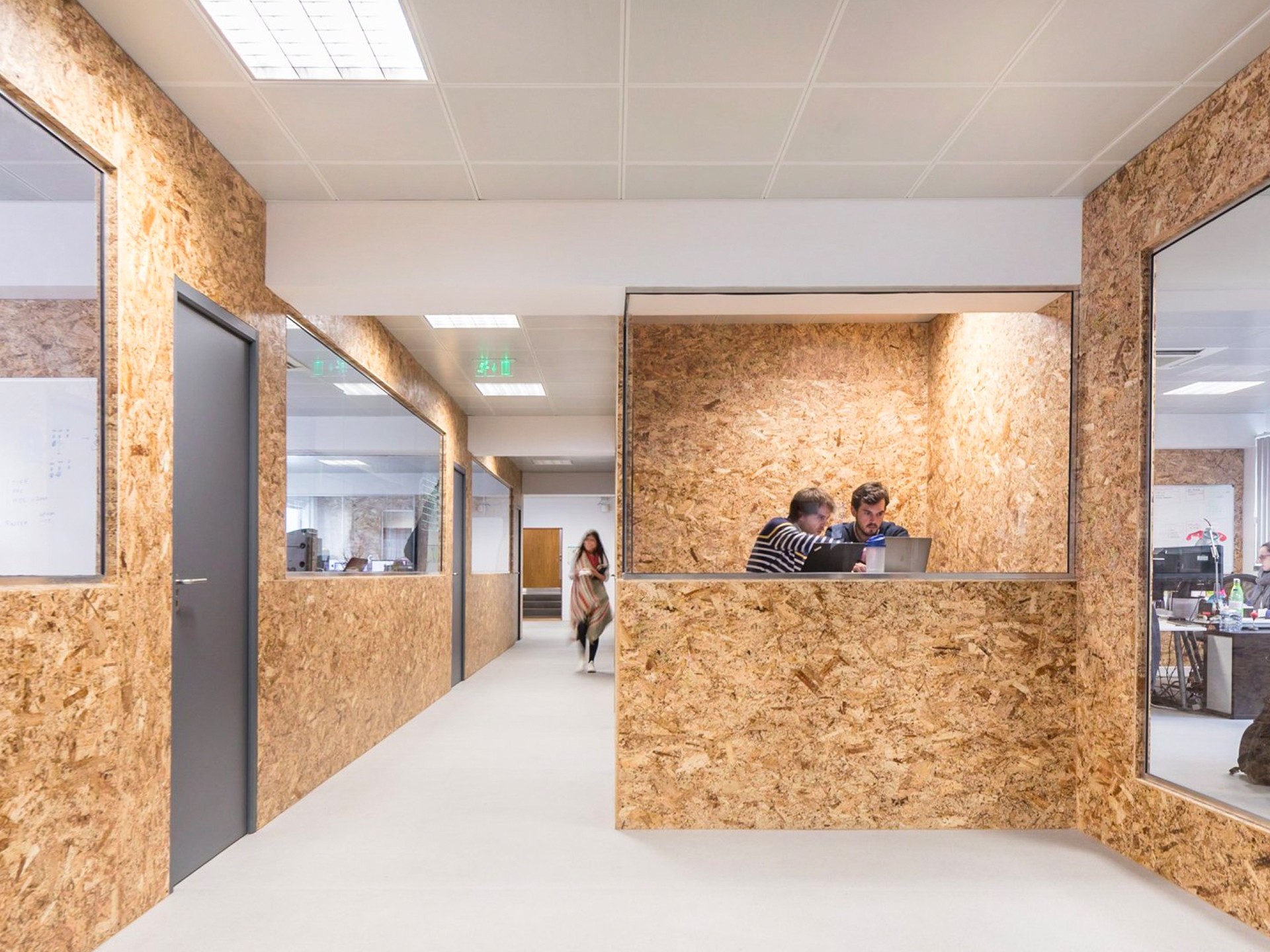 An empty and long hall at Premium Minds' office. There's a small lounge, with couches and a small table with a plant on it, and multiple doors and windows to the various development teams' working areas.