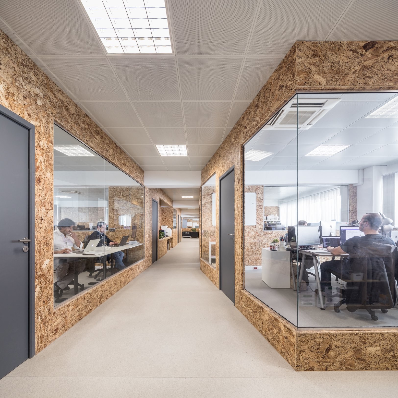 An empty and long hall at Premium Minds' office. There's a small lounge, with couches and a small table with a plant on it, and multiple doors and windows to the various development teams' working areas.