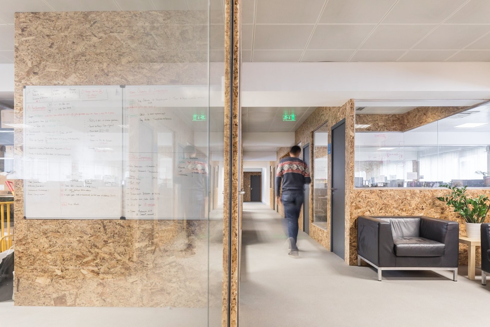 An empty and long hall at Premium Minds' office. There's a small lounge, with couches and a small table with a plant on it, and multiple doors and windows to the various development teams' working areas.